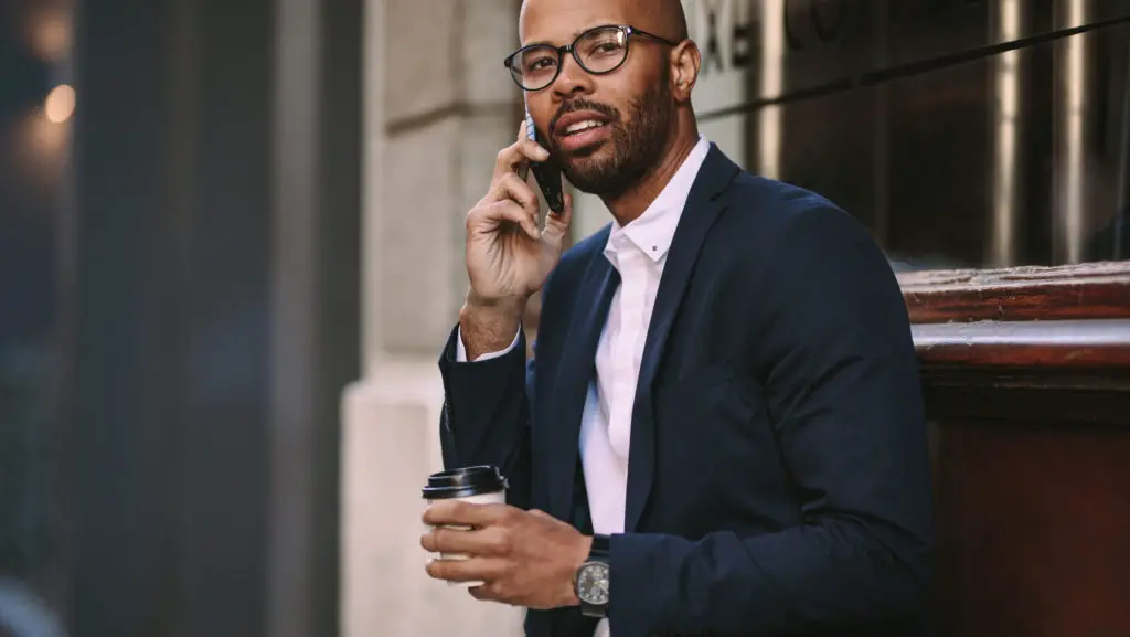 Business man in suit on expensive smartphone outside office building.