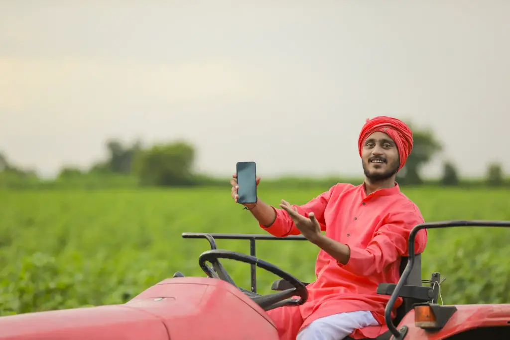 Indian farmer holding smartphone on tractor knowing he's using a safe alternative to MMS