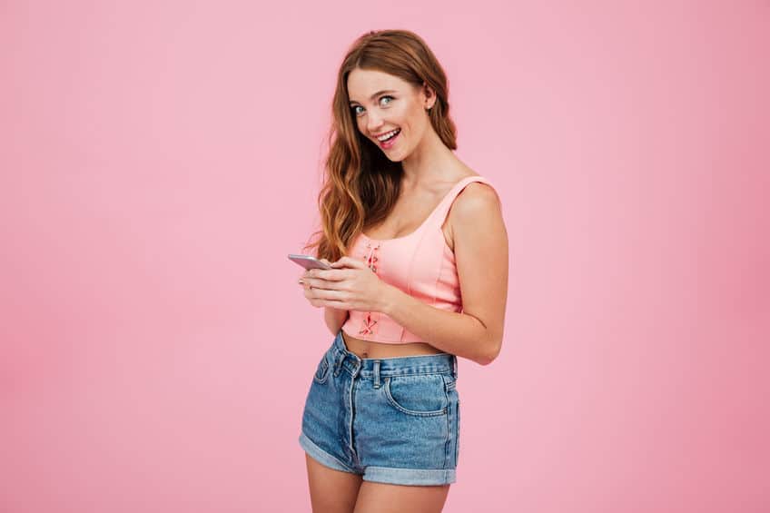 Smart smiling woman in summer clothes holding mobile phone confident that she knows how to send a disappearing photo