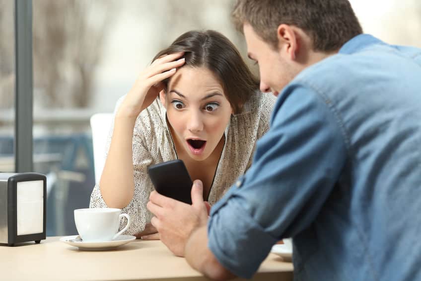 Man showing surprised woman a text message on his smartphone making us wonder "how do you send a disappearing text message".