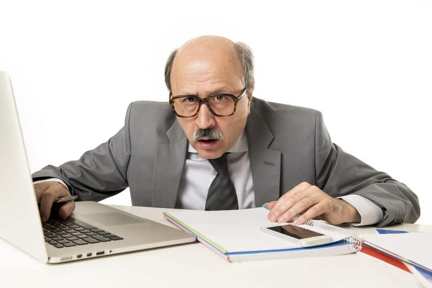Older businessman with laptop, phone, notebook, and a confused expression as he asks: is gmail the same as email?