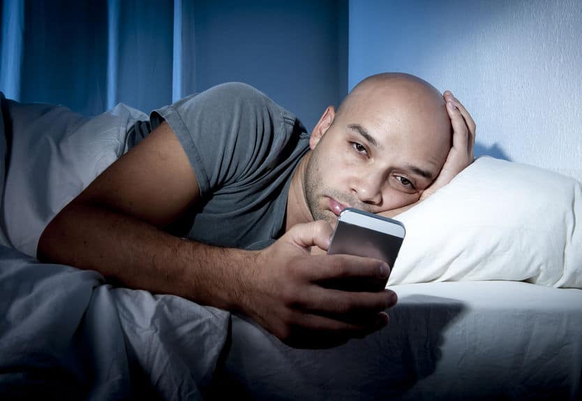 Man using smartphone in bed realizing he needs to quit social media and stop using it so much