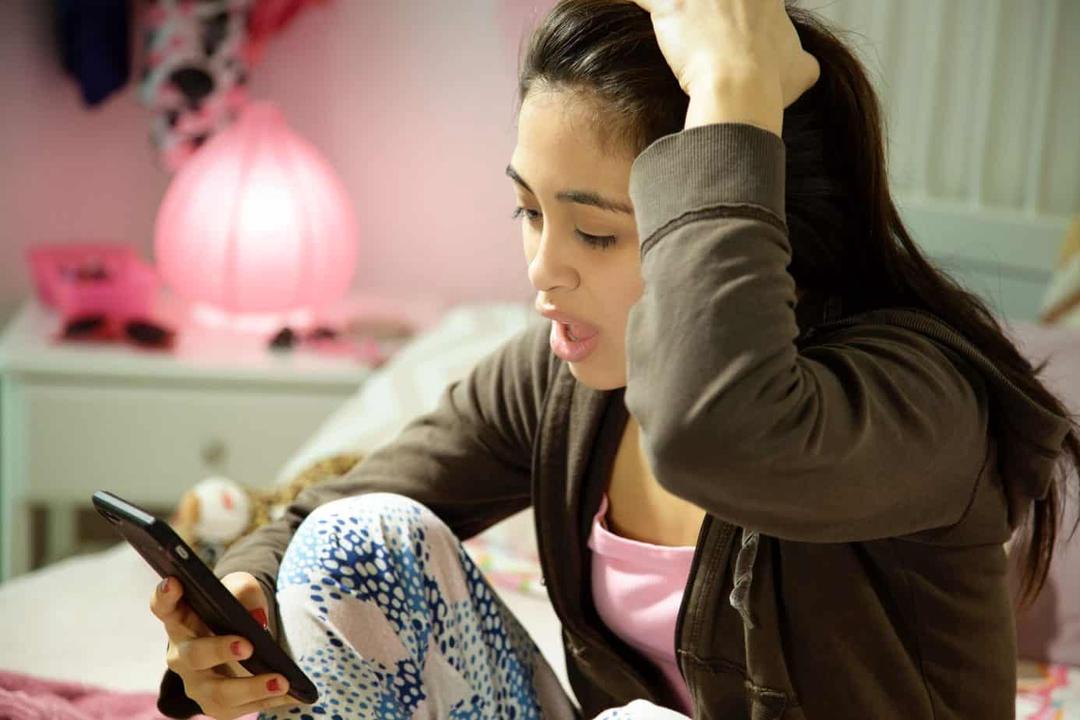 Teenage girl with smartphone wondering the origin of cyberbullying