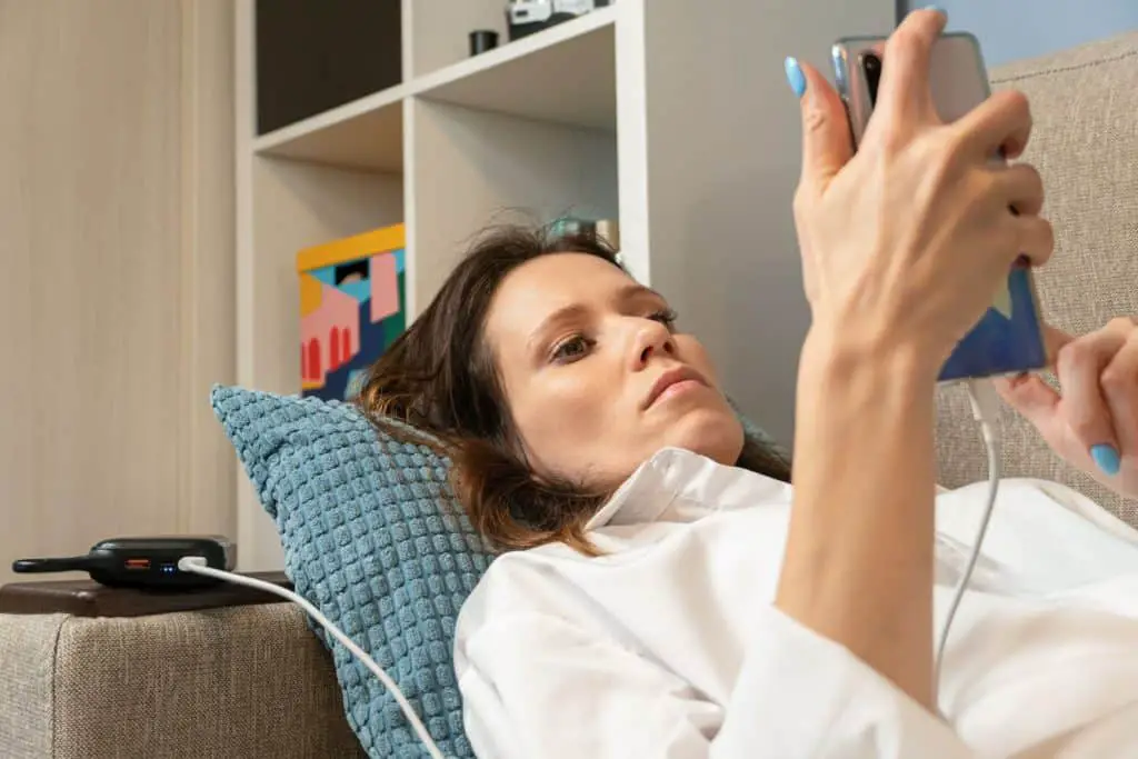 Woman using smartphone while charging with battery pack to maximize battery life expectancy