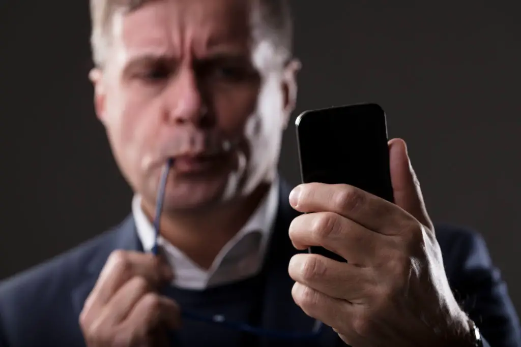 Worried man chewing glasses staring at smartphone after receiving a phishing link