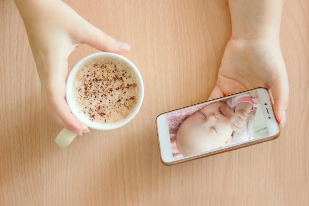 Woman holding a coffee and smartphone which she's using as a baby monitor since her phone is without a sim card