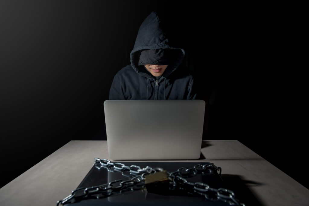 Hooded hacker breaking into a chained laptop which has open source antivirus