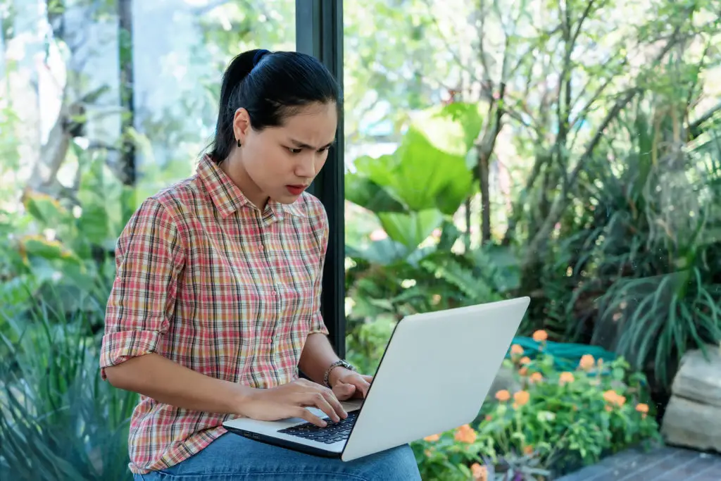 Concerned woman in garden with a laptop on her knee wondering if open source antivirus is necessary