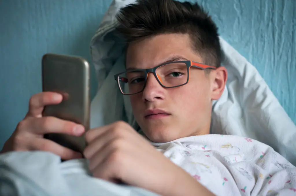 Teen in bed holding smartphone wondering is mms safe