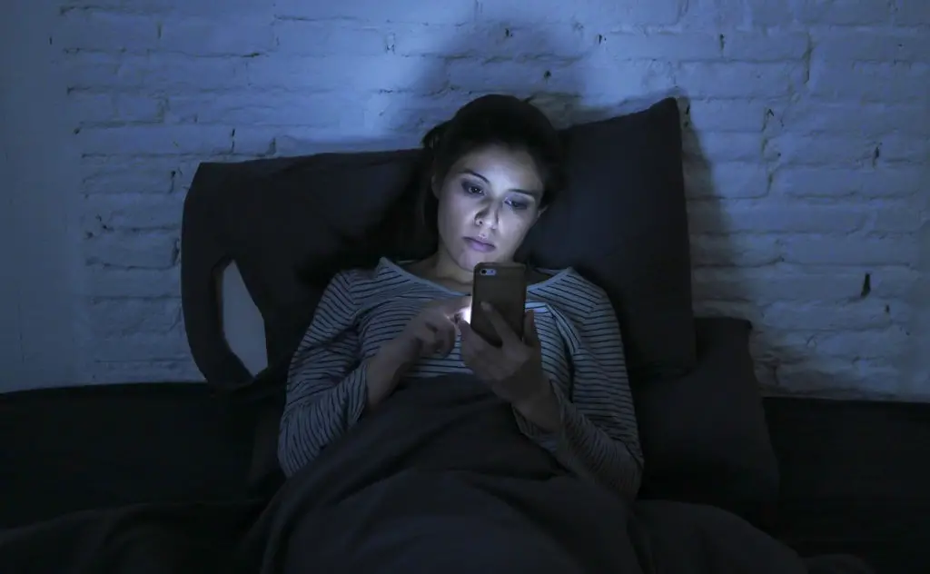 Woman using smartphone in the dark in bed while her phone gets hot