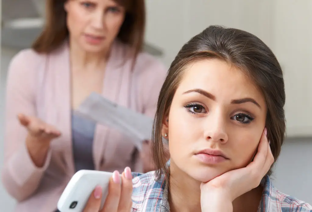 Parent in background holding bill while teen with smartphone worried if you can see search history on the phone bill
