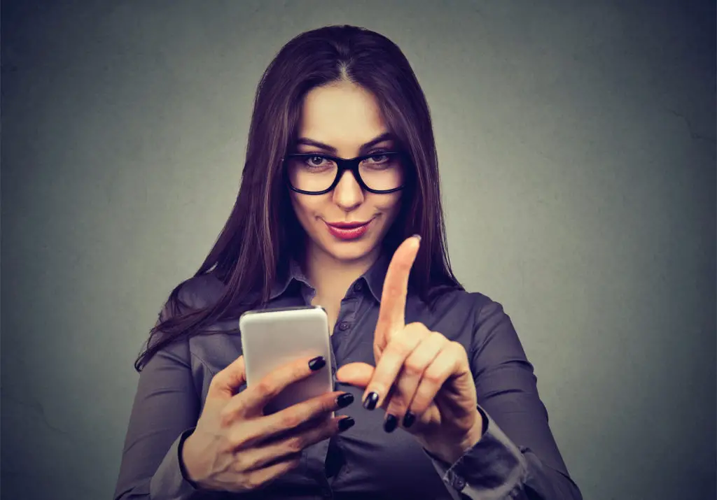 Woman with glasses wagging her finger at adblockers while holding her cell phone.