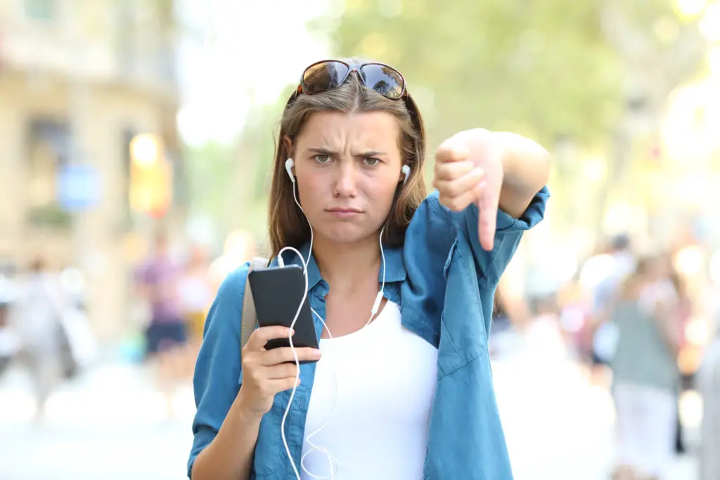 Annoyed woman listening to music with thumbs down in the street.
