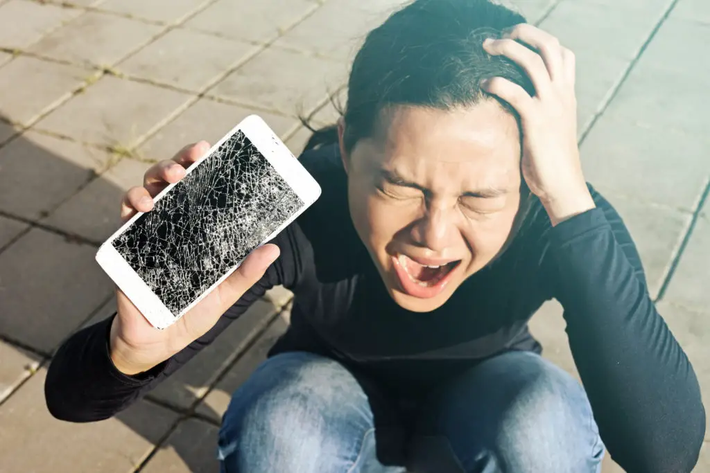 Woman screaming in frustration over cracked screen of expensive smartphone.