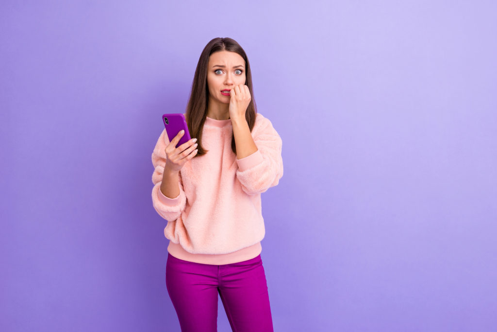 Woman biting nails holding purple phone wondering how to make a fake number for whatsapp.