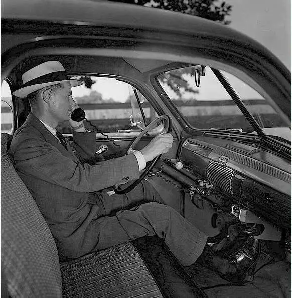 1950s man in hat using a corded car phone.