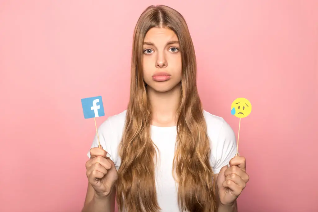 Sad woman holding sticks with facebook logo and crying emoji wondering what are the best facebook privacy settings