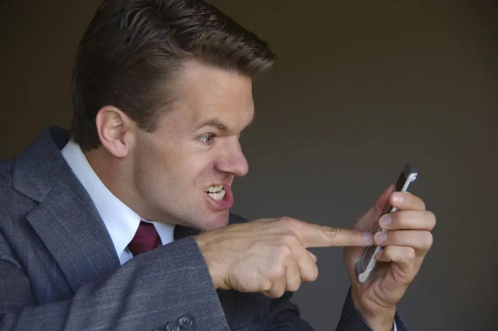 Man in suit pointing angrily at his cell phone.