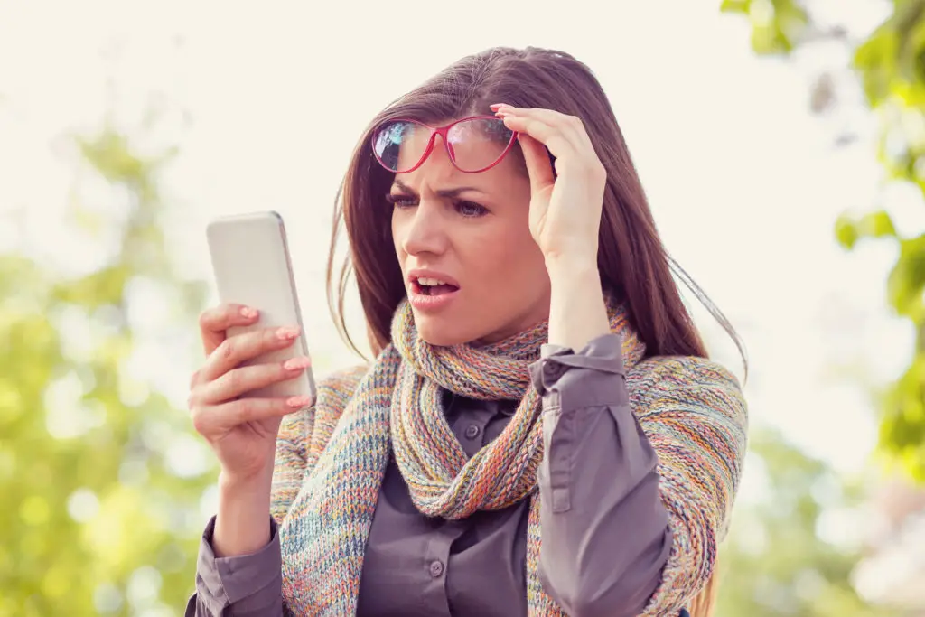 Confused woman with glasses holding smartphone because her whatsapp account was hacked via call forwarding