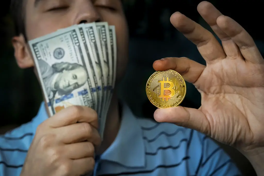 Man holding bitcoin in one hand and cash in the other.