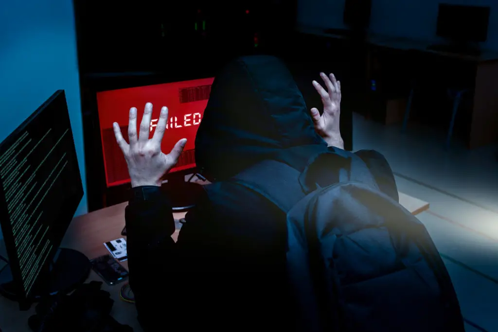 Hacker in hoodie with hands up in surrender in front of screen that says "failed".