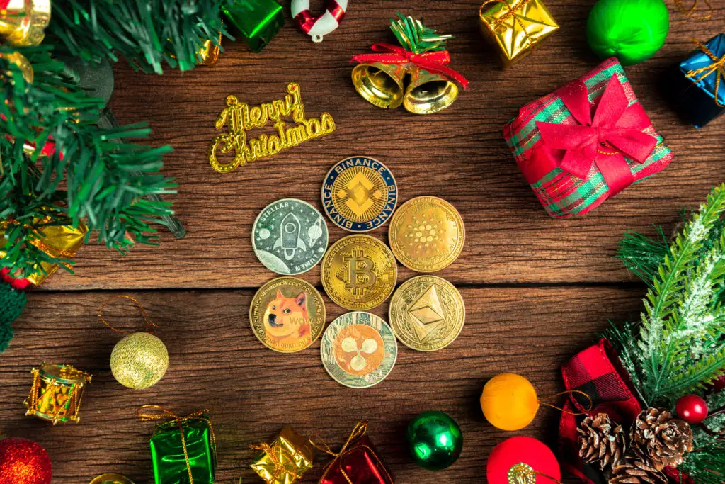 Several different cryptocurrency coins under a christmas tree with other gift boxes.