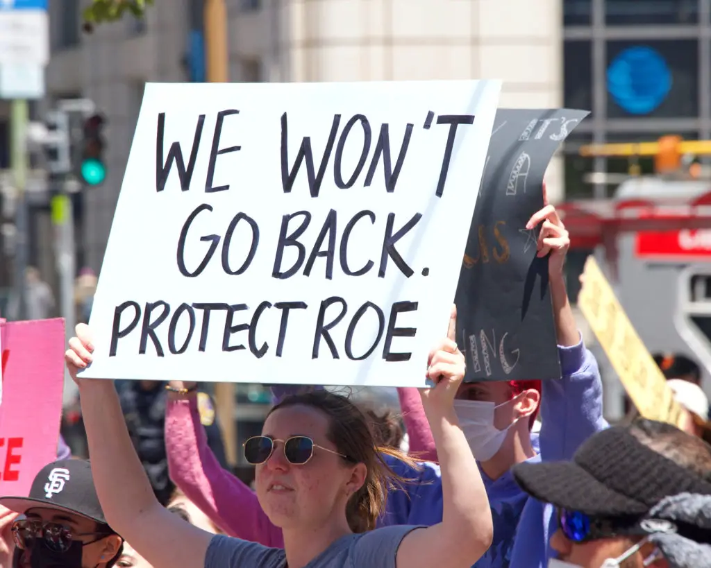 Woman at women's rights protest holding sign that says "we won't go back. Protect roe. "