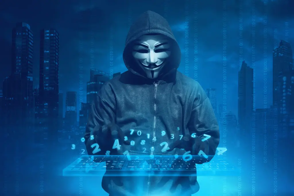 Person in hoodie and anonymous mask with a keyboard and numbers floating around to hack a password.