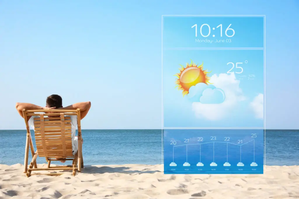 Man sitting in chair on the beach with an image of a weather app showing 25 degrees celsius.
