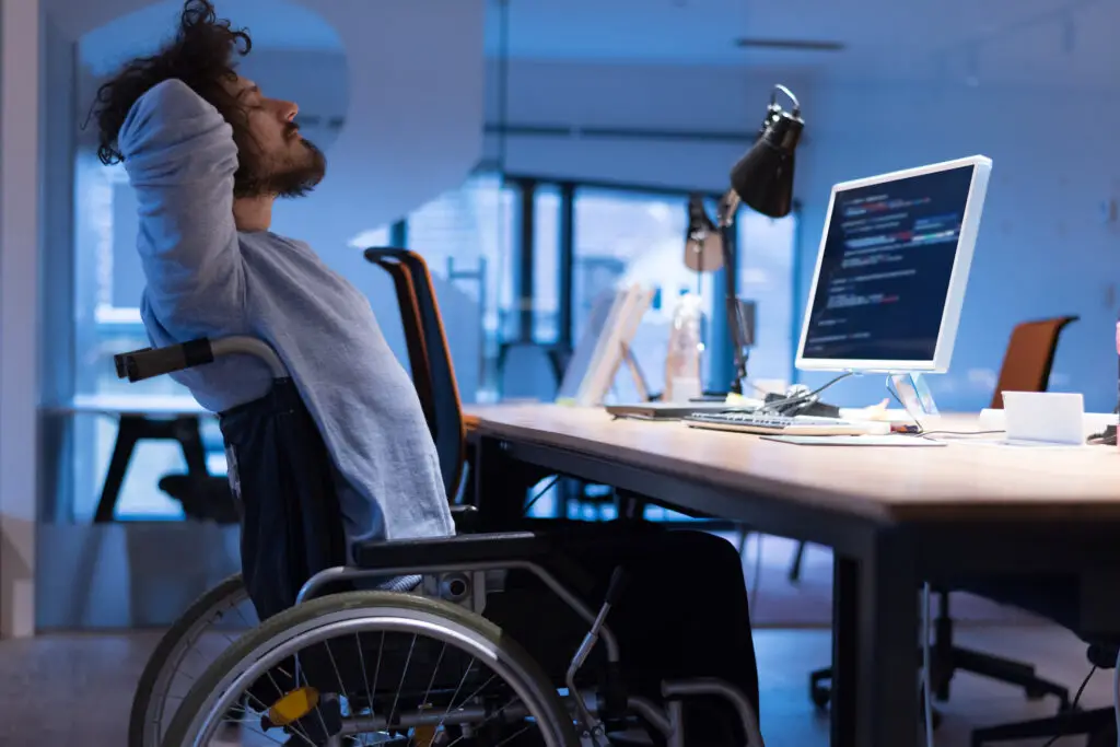 Man in a wheelchair at a desk with code on the screen as he works as a web developer