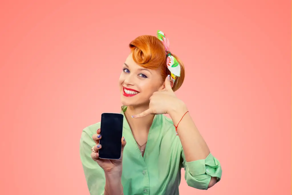 Retro, red-haired woman with cell phone making "call me" symbol with her fingers by her ear.
