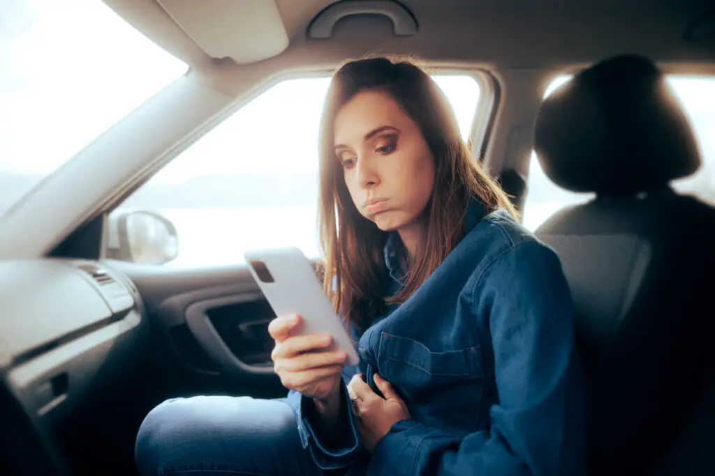 Woman in passenger seat of a car looking at her android phone trying to figure out how to recover her deleted text messages.