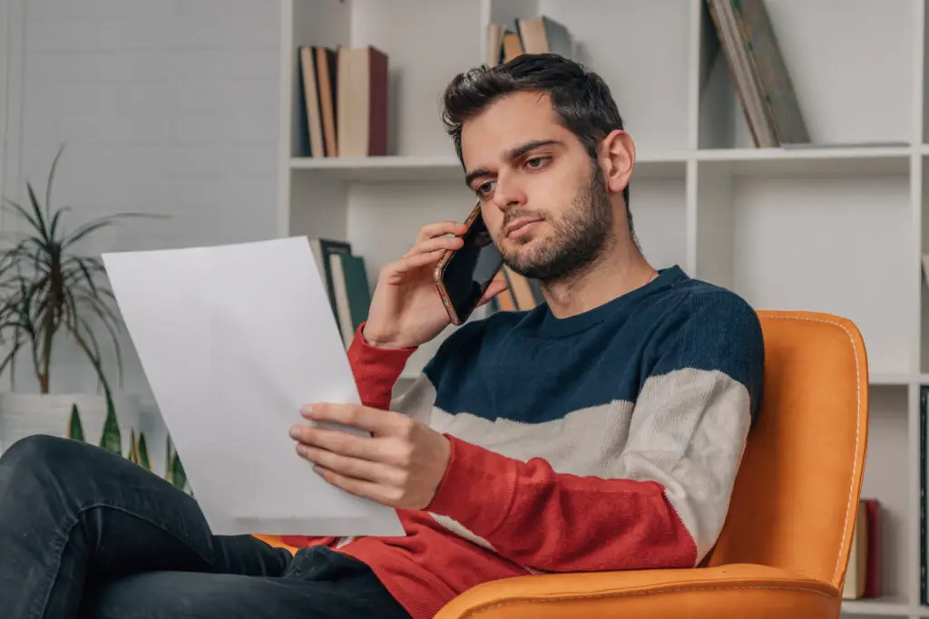 Indian man sitting studying phone bill while talking on the phone