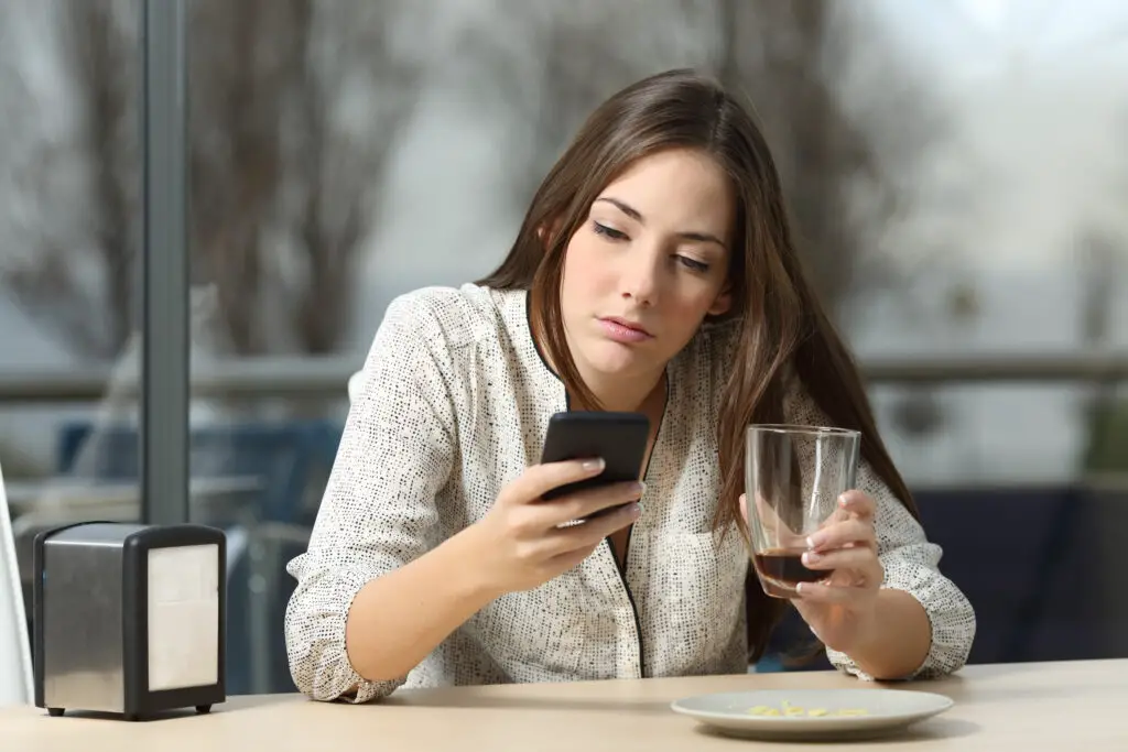 Annoyed woman in coffee shop searching how to recover the messages she accidentally deleted on her phone