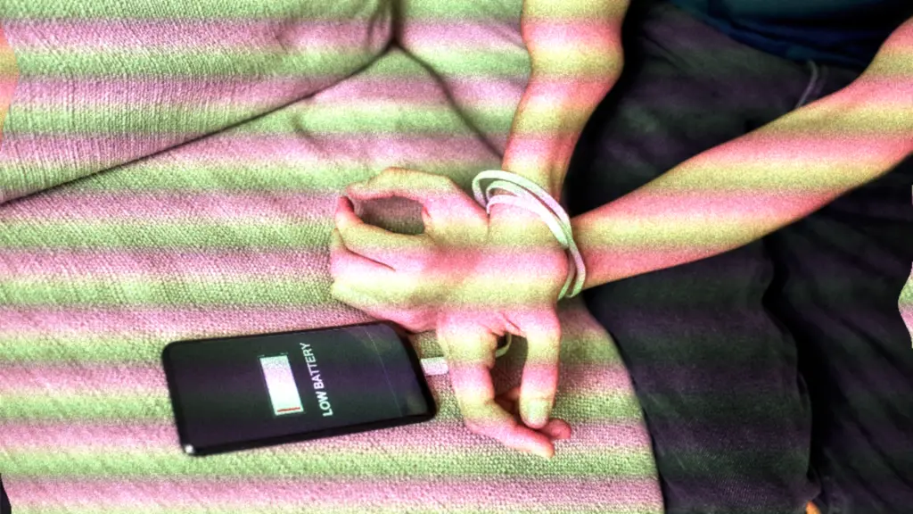 Smartphone displaying "low battery" with charging cable used to tie person's hands