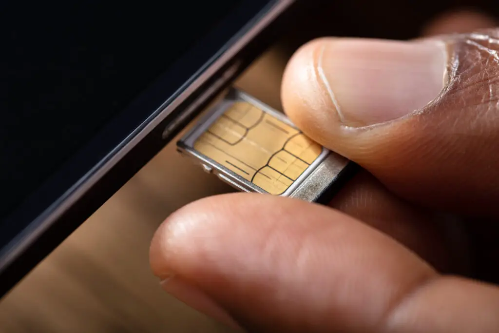 Close-up photo of a person removing a sim chip from a smartphone considering how often should a sim card be replaced