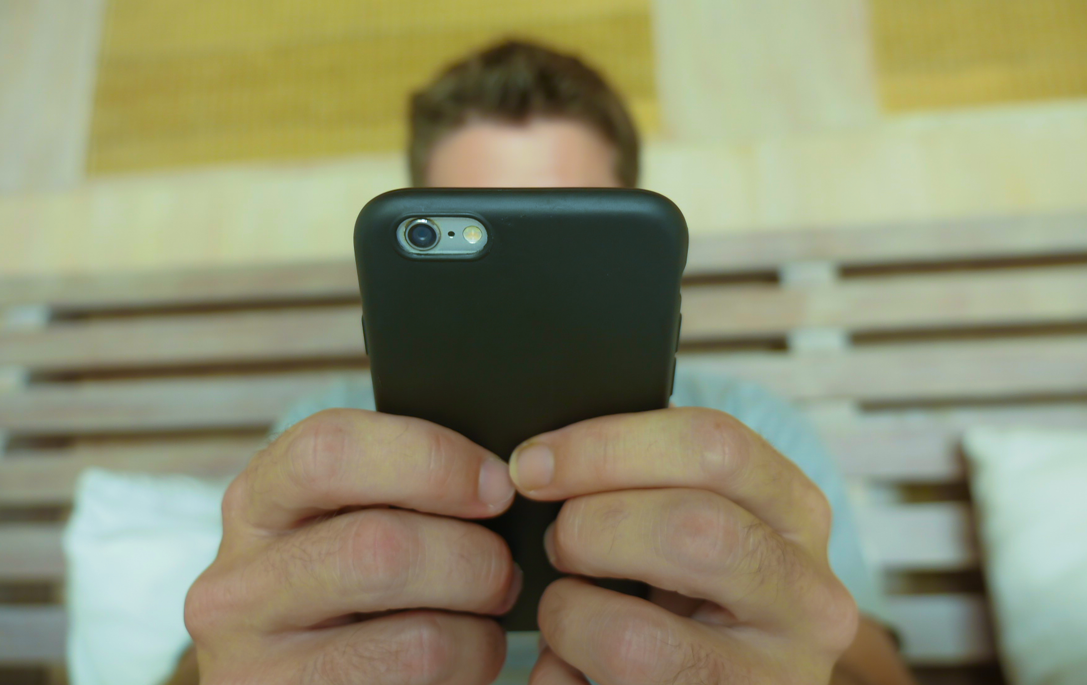 Man holding a smartphone which covers his face as he sends an anonymous text