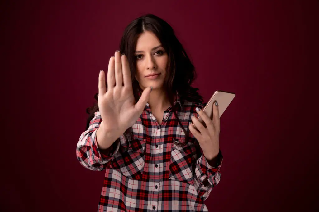 Girl with smartphone holding up her hand now knowing: is it better to block or delete spam
