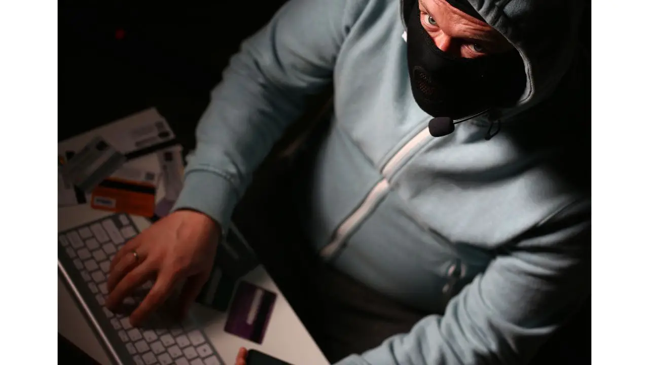 A menacing hacker, wearing a mask and exuding a ruthless demeanor, demonstrates the misuse of stolen information for identity theft and financial fraud. With credit cards in hand, this individual showcases the alarming reality of online security breaches and the potential consequences of personal data falling into the wrong hands.
