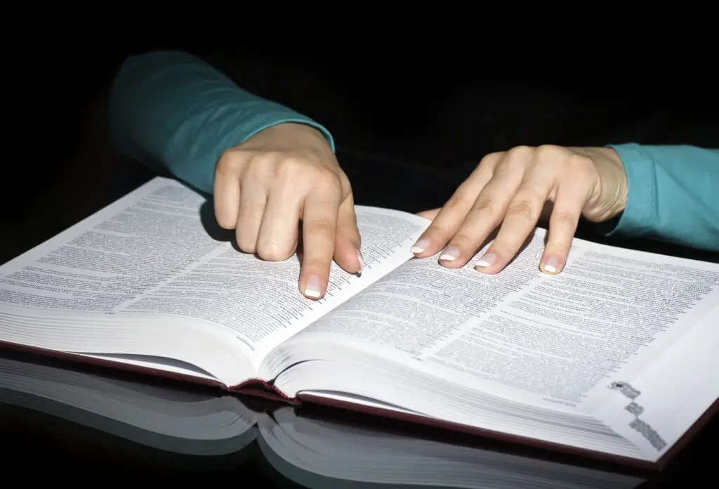 Hands pointing at an entry in a reference book, illustrating the search for password generator words