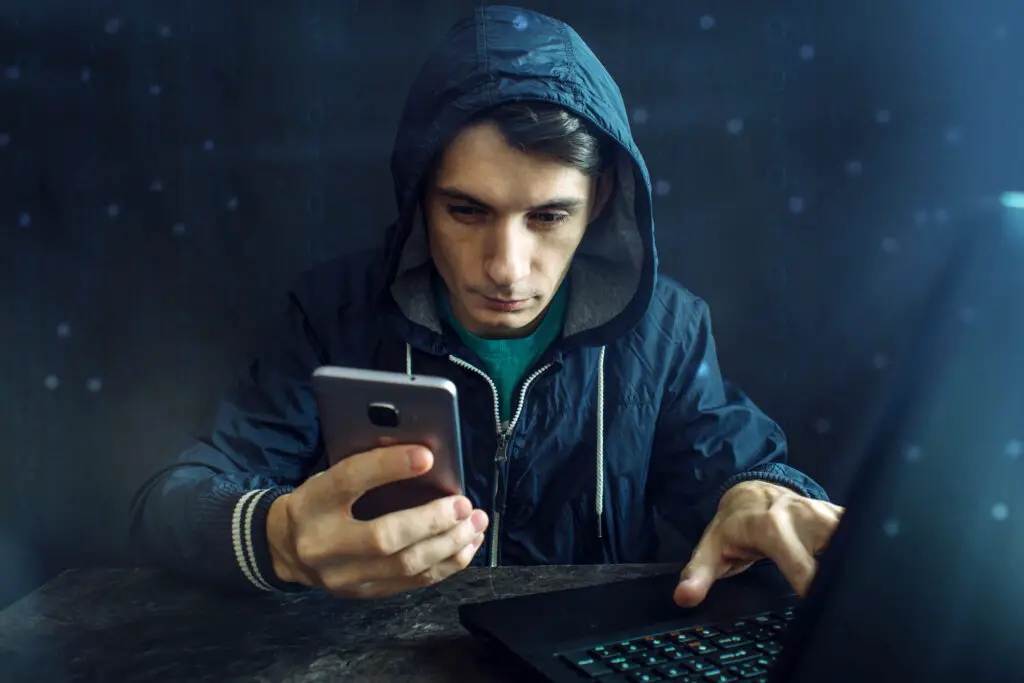 Hacker holding smartphone answering the question: can you get hacked by texting a number back
