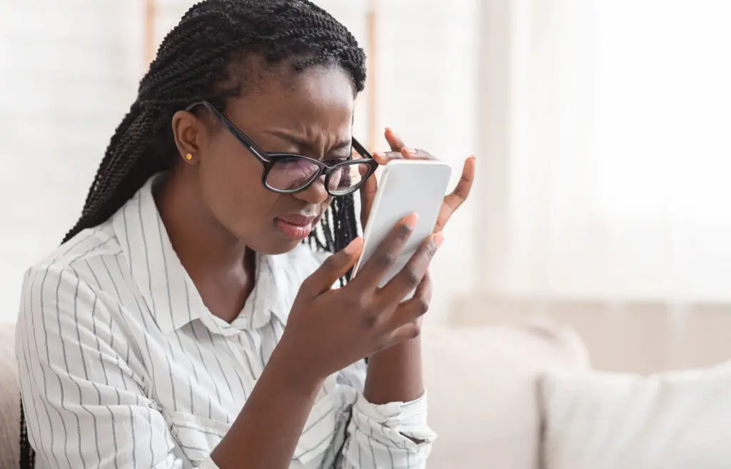 Woman with glasses squinting and wondering how far away should you hold your phone