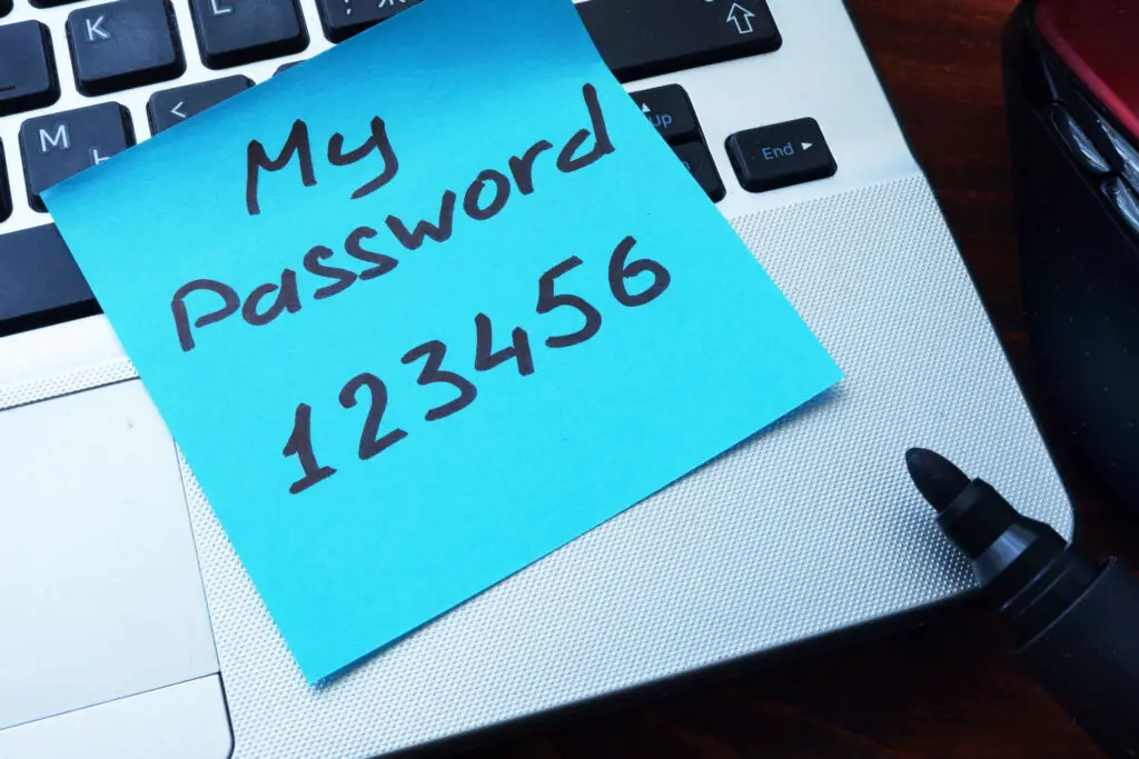 Sticky note on a laptop showing a weak password with 6 characters